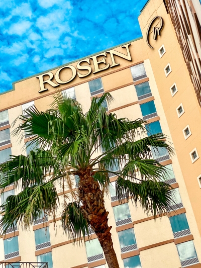 A close-up shot of the word "Rosen" on the side of Rosen Plaza Hotel, with a palm tree in the foreground.