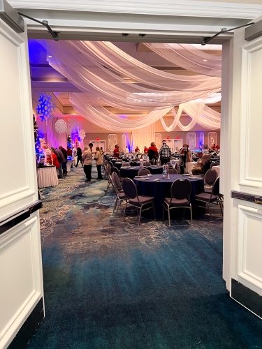 Double doors opening into a ballroom with round tables, purple lighting, and white sheer drapery hanging from the ceiling.  Enjoy an elegant Christmas Day buffet at Rosen Plaza in 2024.