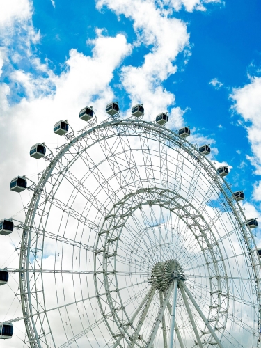 A close up of the Orlando Eye observation wheel against a blue sky with puffy clouds. Riding the Eye is a great thing to do on Thanksgiving in Orlando.