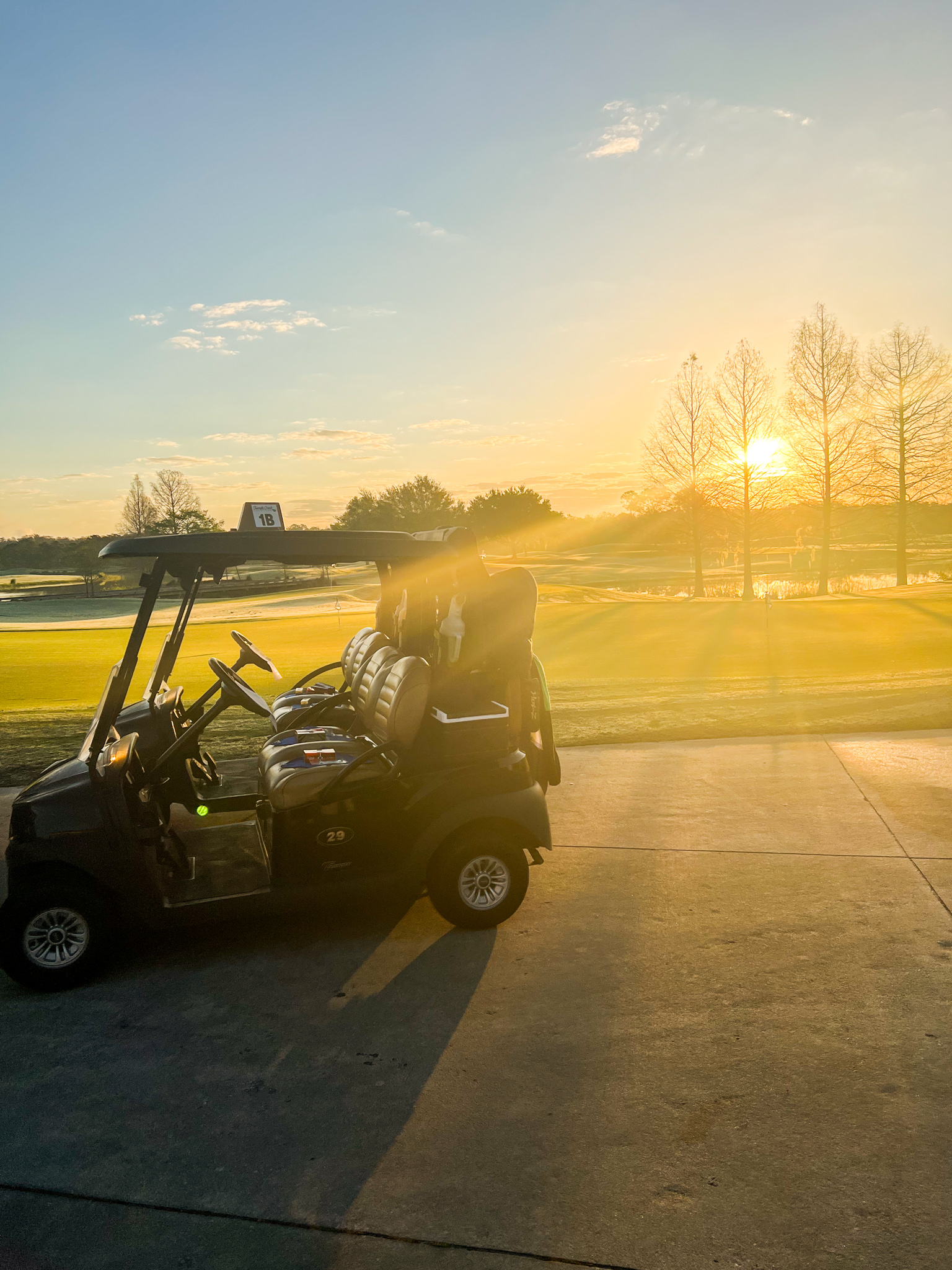 A dark-colored golf cart sits on concrete with a foggy golf course and rising sun in the distance at Rosen Shingle Creek Golf Club.