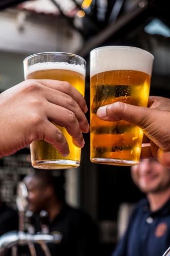 Two hands holding glasses of beer in a toast to their favorite teams at one of these spots for watching sports near International Drive in Orlando.