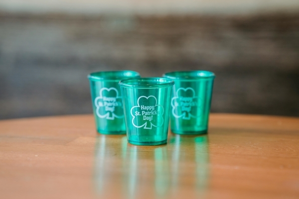  Three green shot glasses with shamrocks that say ”Happy St. Patrick’s Day!” on a wooden table. Enjoy St. Paddy's Day in Orlando