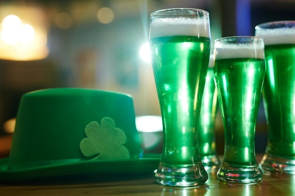 A green hat with a shamrock sits on a table next to four pints of green beer.